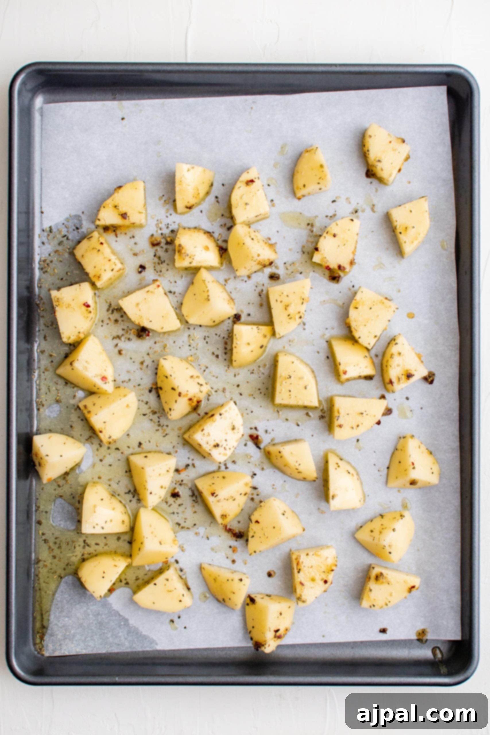 Simple Sheet Pan Sausage Dinner 15 Picture of seasoned potato slices arranged on a baking sheet with parchment paper, ready for initial baking.
