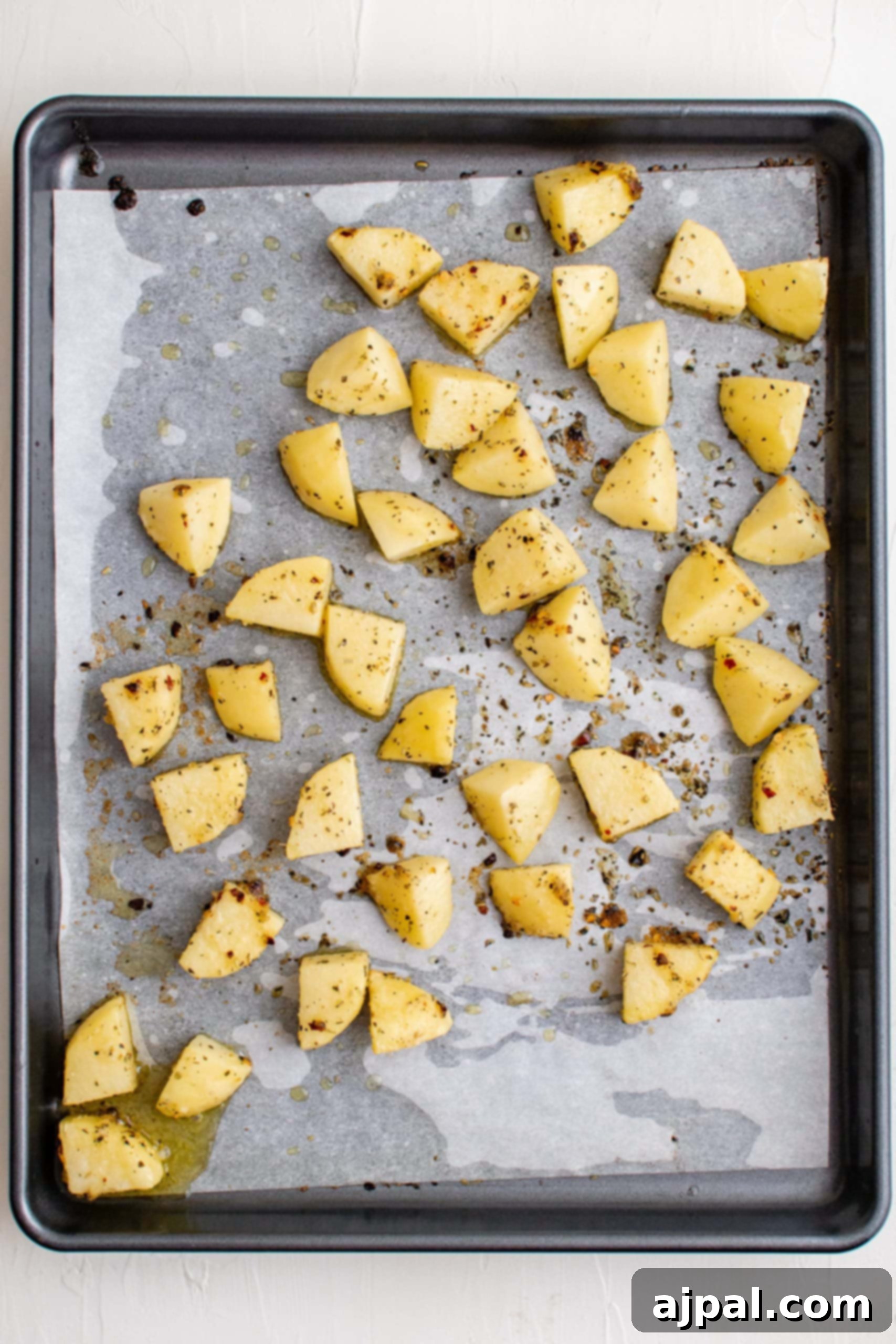 Simple Sheet Pan Sausage Dinner 16 Picture of lightly baked seasoned potato slices on a baking sheet, showing their partial cooking stage.