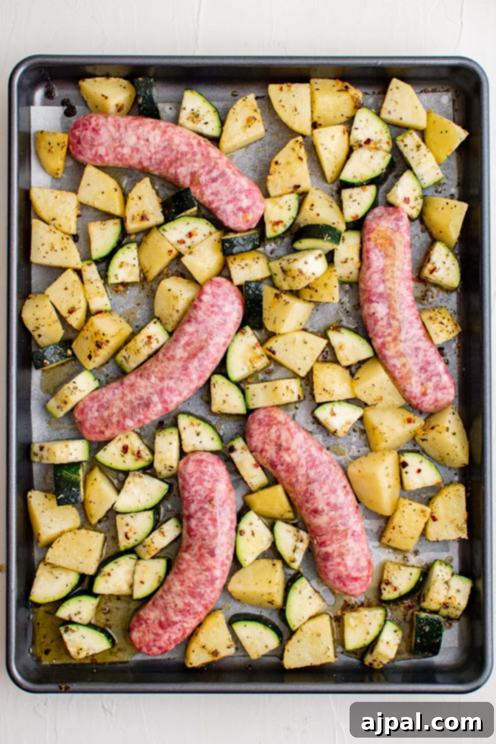 Simple Sheet Pan Sausage Dinner 17 Picture of sausages, zucchinis, and seasoned potato slices on a baking sheet, newly combined for the next stage of baking.