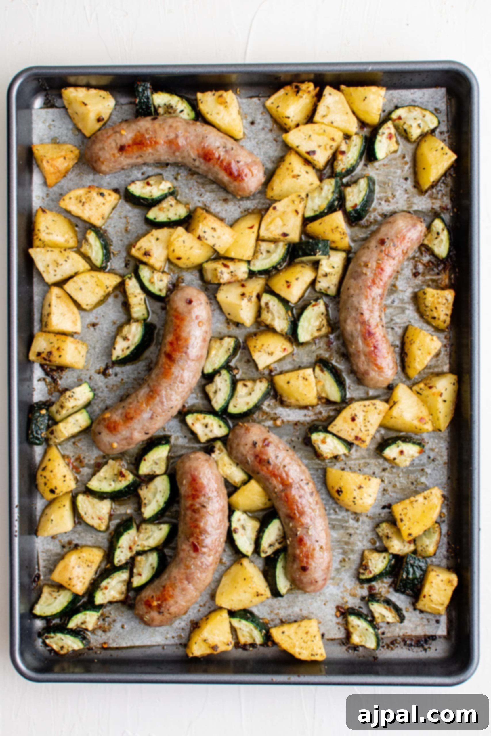 Simple Sheet Pan Sausage Dinner 18 Picture of fully baked sausages, zucchinis, and seasoned potato slices on a baking sheet, golden and delicious.