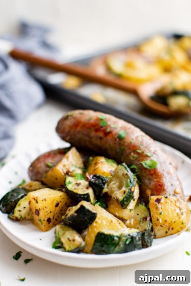 Simple Sheet Pan Sausage Dinner 4 Close-up picture of perfectly roasted sausage, potatoes, and zucchini on a white plate, showcasing the delicious texture and color.