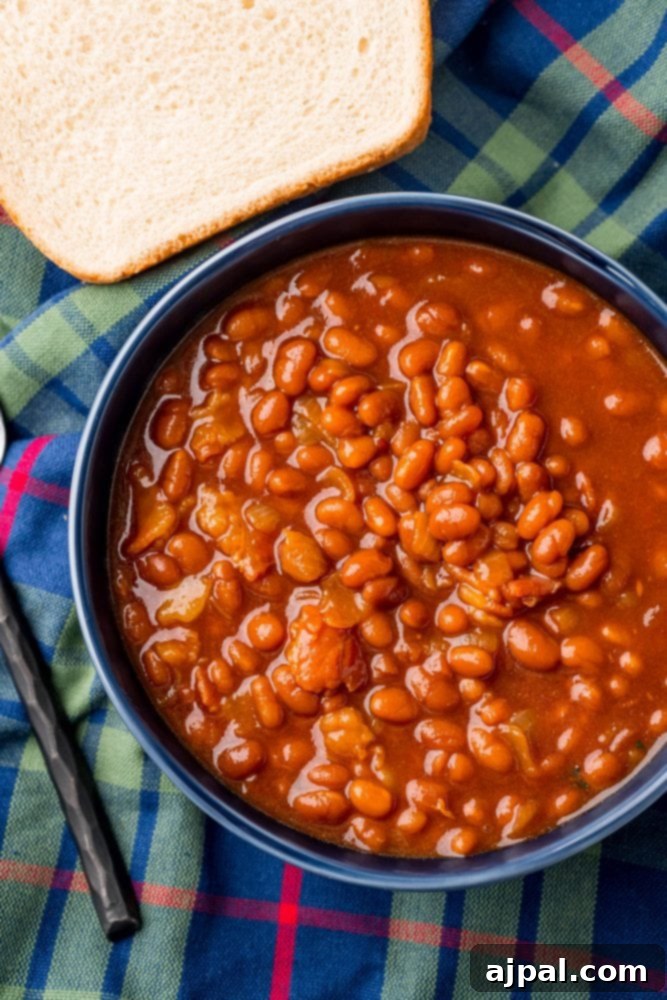 A comforting bowl of slow cooker baked beans, garnished and ready to be enjoyed, with a spoon resting beside it on a wooden table.