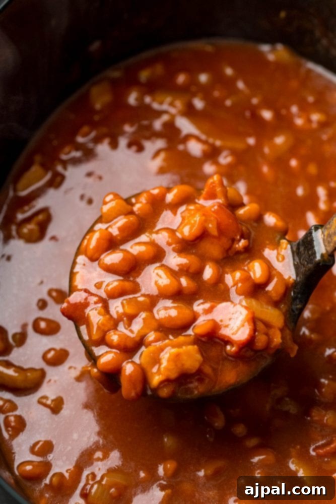 A spoon stirs a delicious batch of slow cooker baked beans, showcasing their rich, thick sauce and tender texture.
