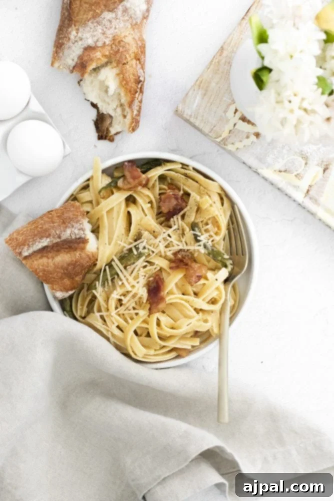 Asparagus Carbonara with Roasted Flair 3 A rustic-style shot of a bowl of carbonara pasta with bacon and roasted asparagus, resting on a white wooden table next to a sprig of fresh herbs.