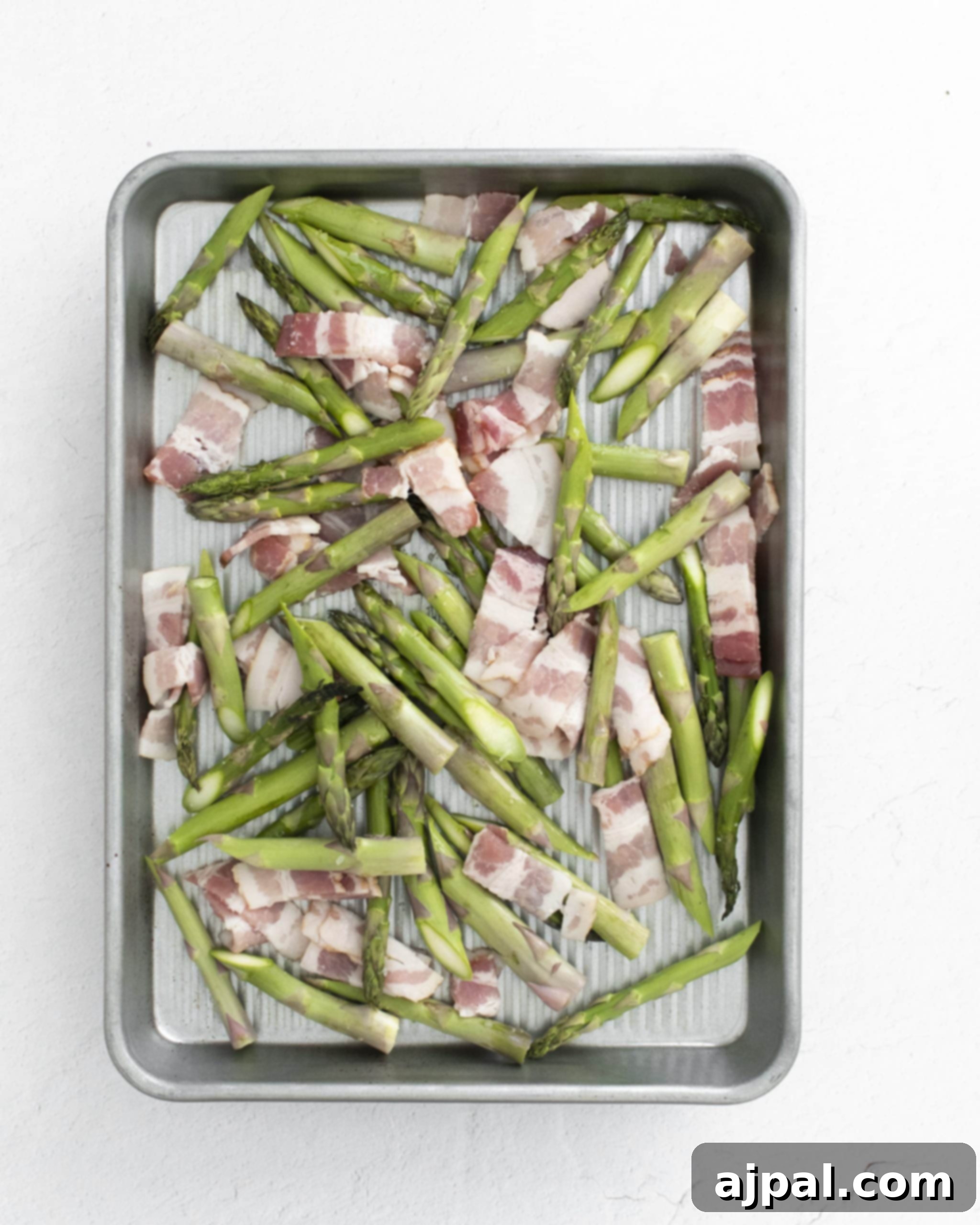 Asparagus Carbonara with Roasted Flair 7 picture of raw chopped bacon and asparagus spears on a baking sheet, ready for roasting