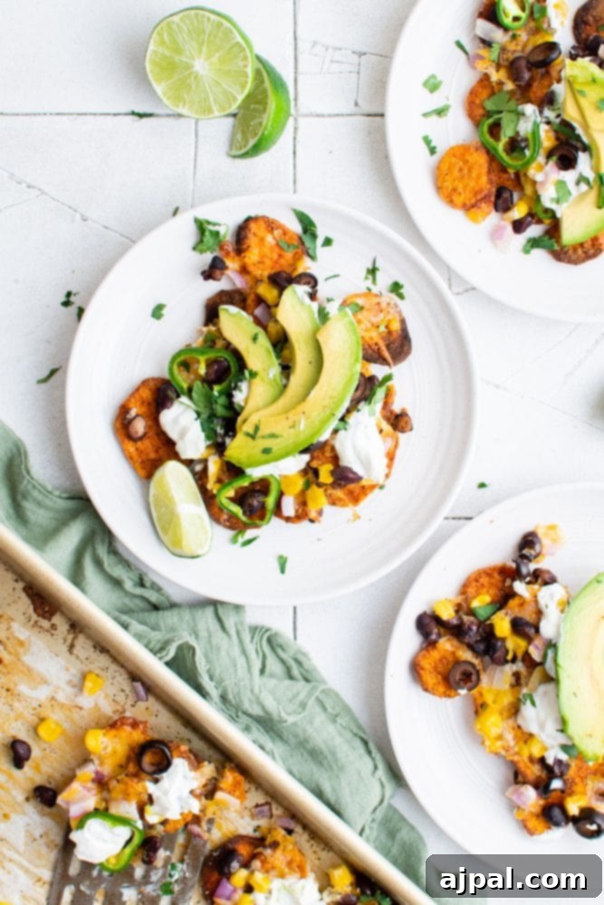 A plate of colorful sweet potato nachos topped with jalapenos, black beans, corn, melted cheese, sour cream, avocado slices, and lime wedges, showcasing a healthy and delicious vegetarian meal.