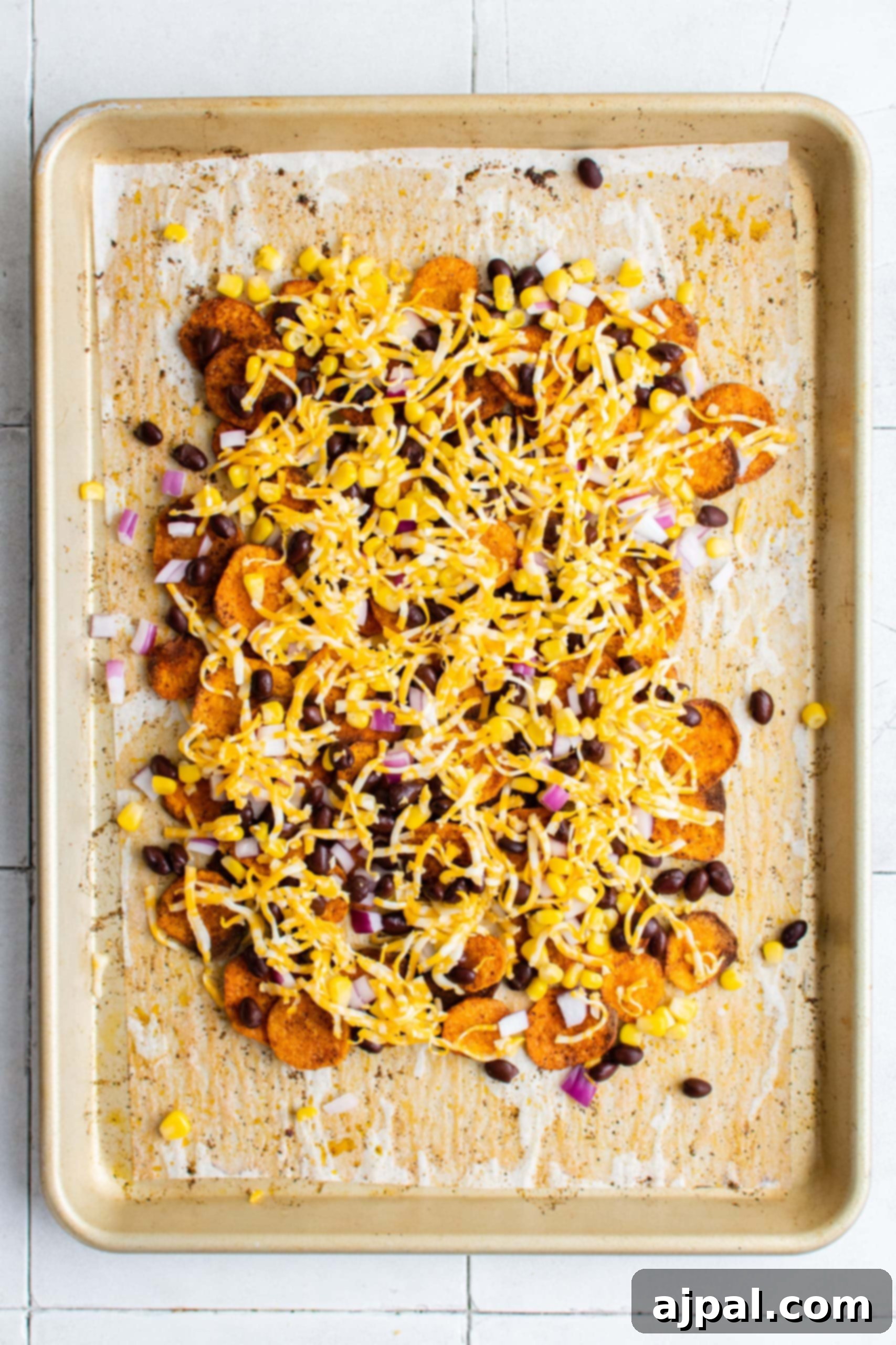 Sweet potato nachos layered with all the vegetarian toppings and a generous amount of cheese, ready for the final bake.