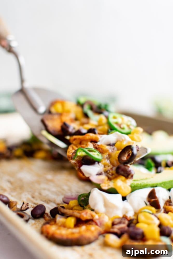A fork lifts a perfectly loaded sweet potato nacho from the plate, highlighting the delicious layers of toppings.
