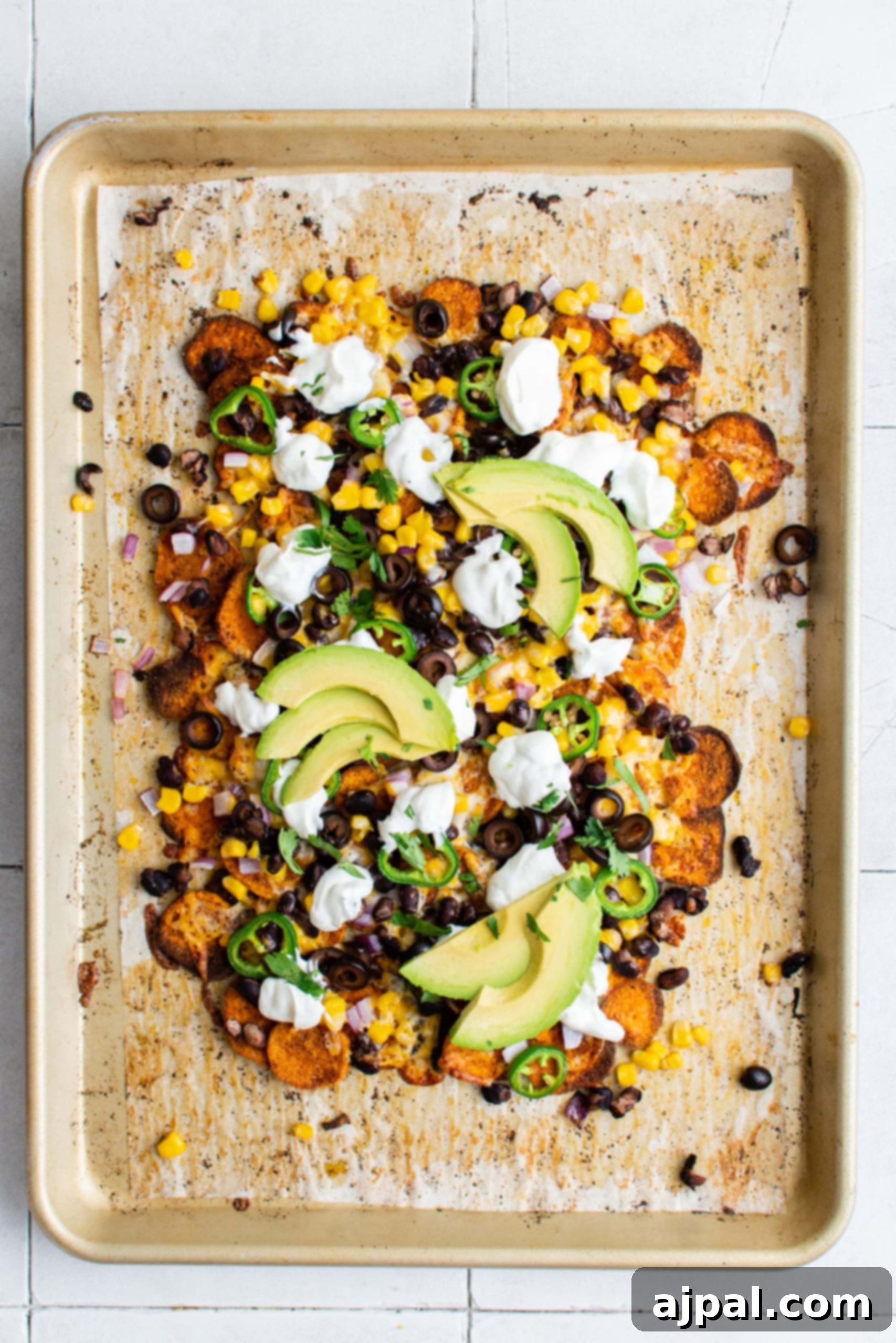 Close-up of sweet potato nachos on a plate with various fresh toppings including jalapenos, beans, corn, cheese, sour cream, and avocados.