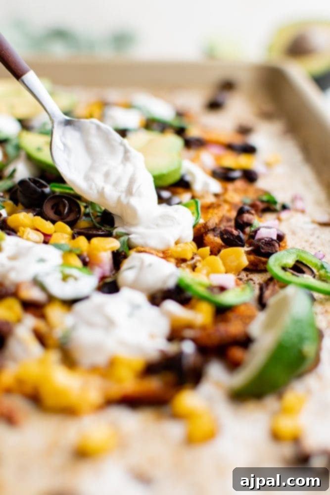 Sheet pan filled with Mexican-style baked sweet potato nachos, showcasing a generous layer of toppings before serving.