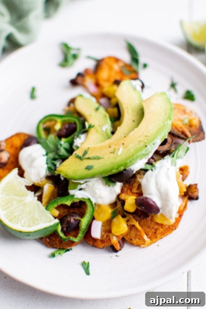 A delicious plate of vegetarian sweet potato nachos, generously topped with creamy avocado slices and a dollop of sour cream, ready to be enjoyed.