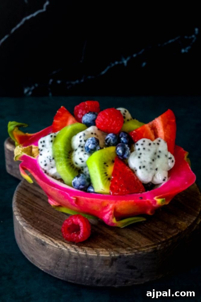 Tropical Dragon Fruit Salad 4 Picture of a colorful diced fruit salad nestled in a carved out dragon fruit hull, placed on a rustic wooden plate.