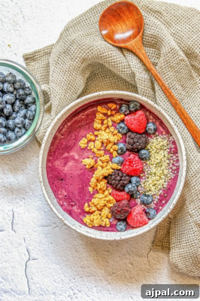 Triple Berry Smoothie Bowls 5 A vibrant and appetizing triple berry smoothie bowl, generously garnished with fresh raspberries, blueberries, and a sprinkle of crunchy granola and hemp hearts, with a wooden spoon nestled in.