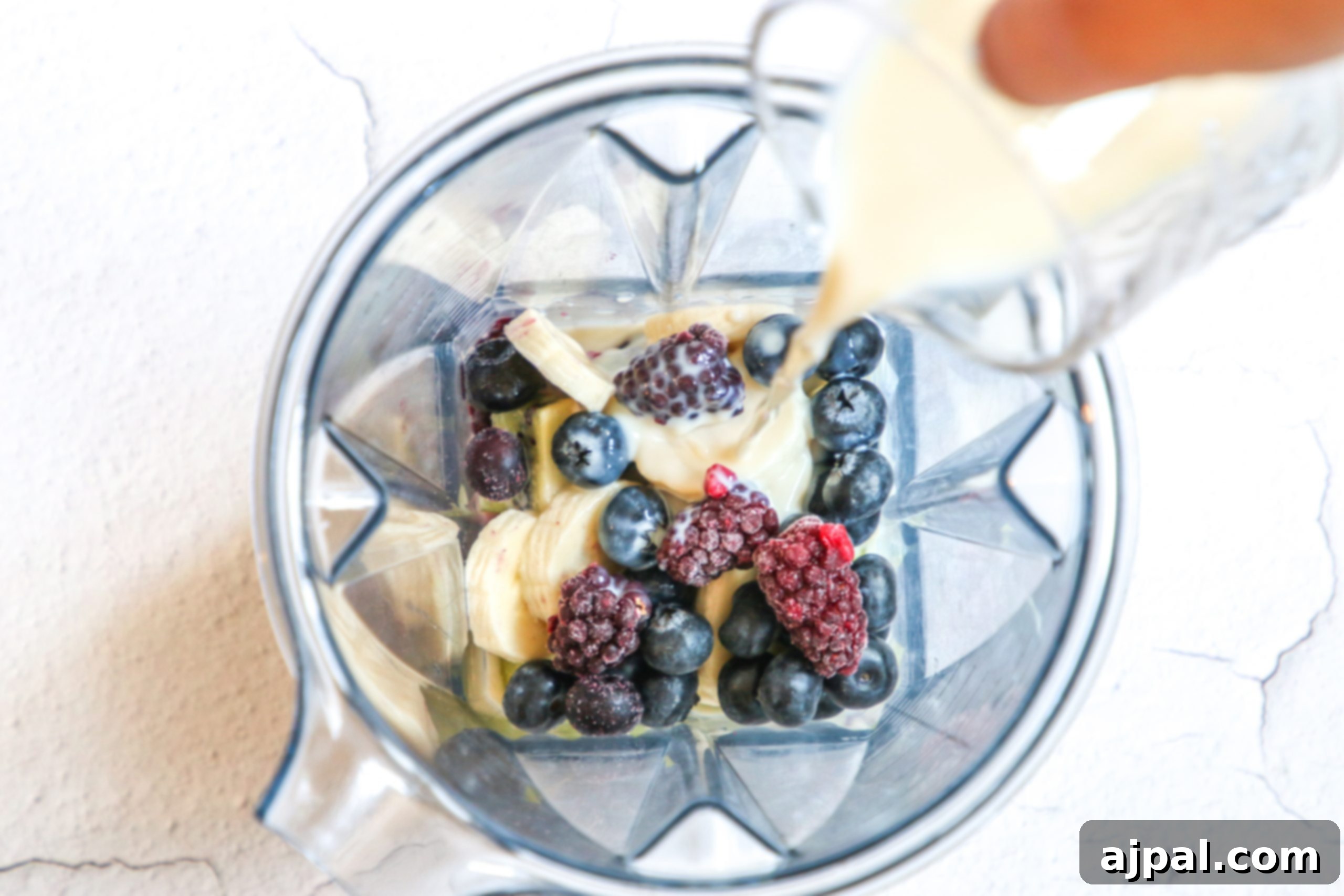 Triple Berry Smoothie Bowls 9 Almond milk is poured into a blender, joining frozen banana and berries, to create a smooth and creamy triple berry smoothie bowl.