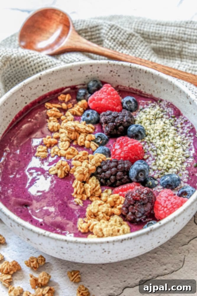 Triple Berry Smoothie Bowls 3 A close-up shot of a vibrant triple berry smoothie bowl, richly topped with an assortment of fresh berries, golden granola, and tiny hemp hearts, ready to be enjoyed.