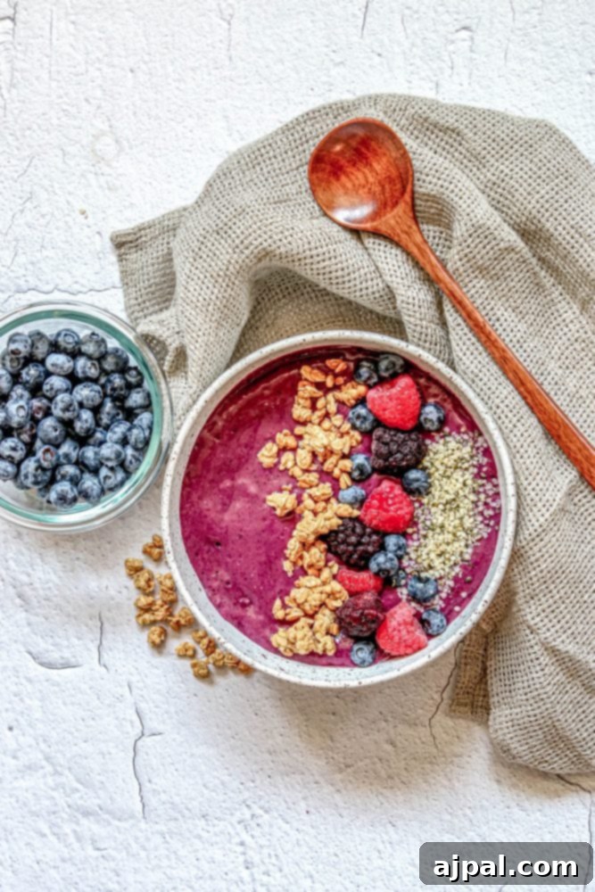 Triple Berry Smoothie Bowls 4 A beautifully composed berry banana smoothie bowl, adorned with a variety of fresh berries and crunchy granola, elegantly presented with a wooden spoon.