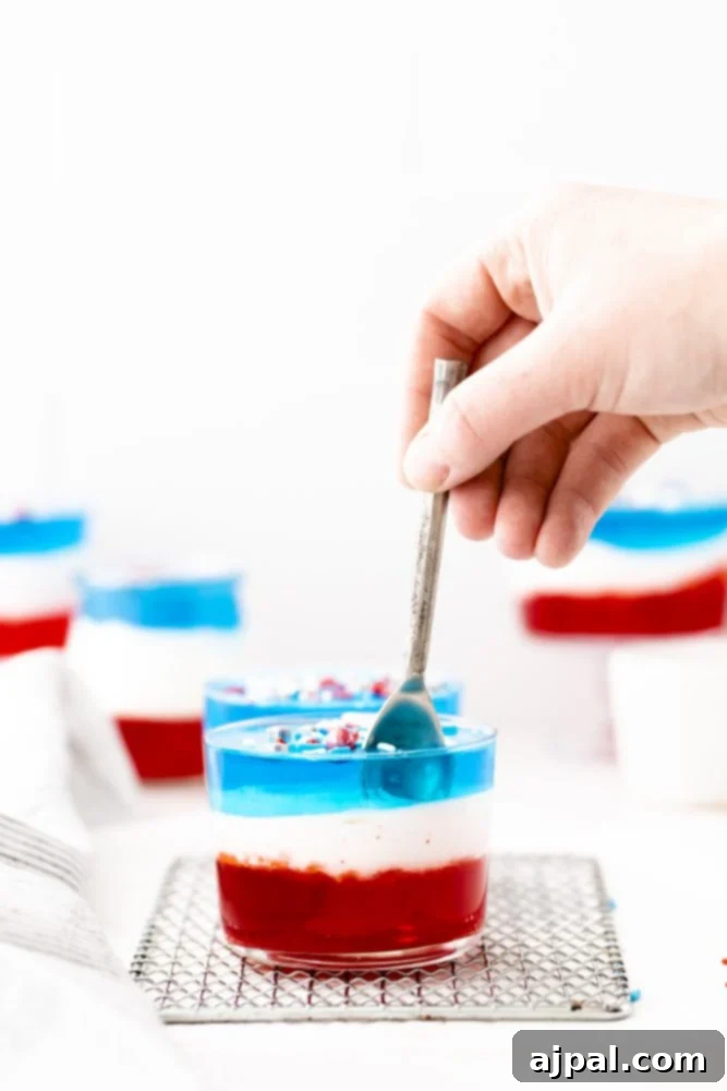 Star-Spangled Jello Cups 2 A person preparing Fourth of July jello cups by dipping a spoon into red, white, and blue jelly.