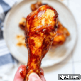 A hand holding an air fryer BBQ chicken drumstick gleams with a savory glaze