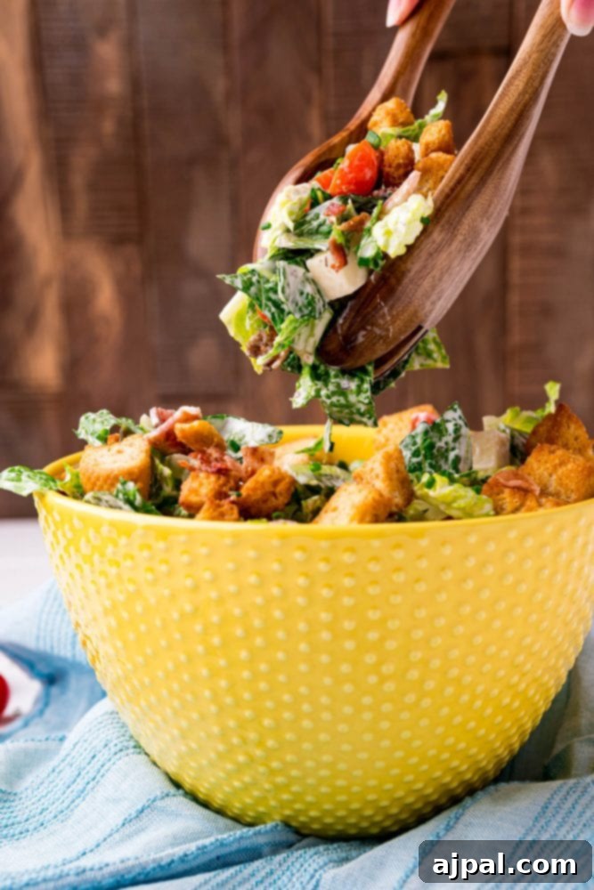 Effortless BLT Salad 3 A person is scooping a bacon tomato salad out of a yellow bowl.