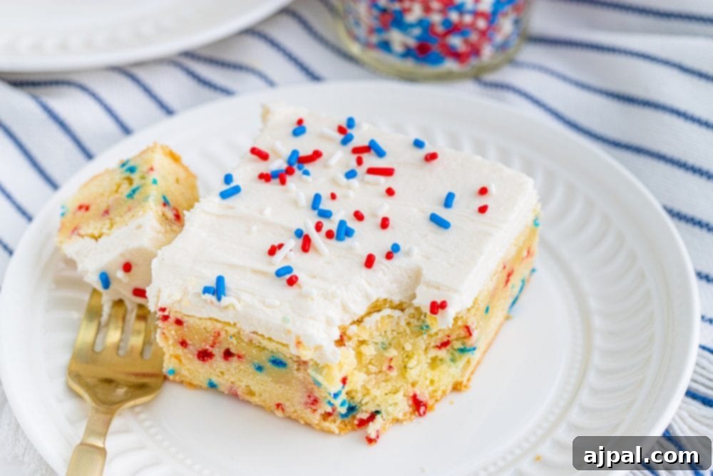 Stars and Stripes Sugar Cookie Bars 3 A single vanilla sugar cookie bar, topped with a generous layer of white frosting and an abundance of patriotic red and blue sprinkles, ready to be enjoyed.