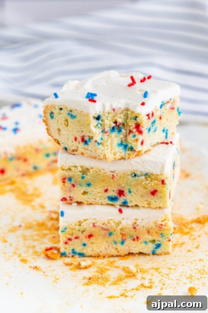 Stars and Stripes Sugar Cookie Bars 5 A stack of patriotic sugar cookie bars, each with creamy white frosting and scattered red and blue sprinkles, ready for serving at a festive occasion.