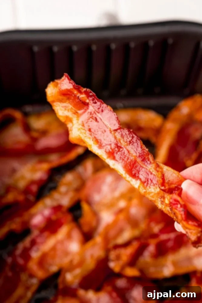 A hand holding a perfectly crispy strip of air-fried bacon.