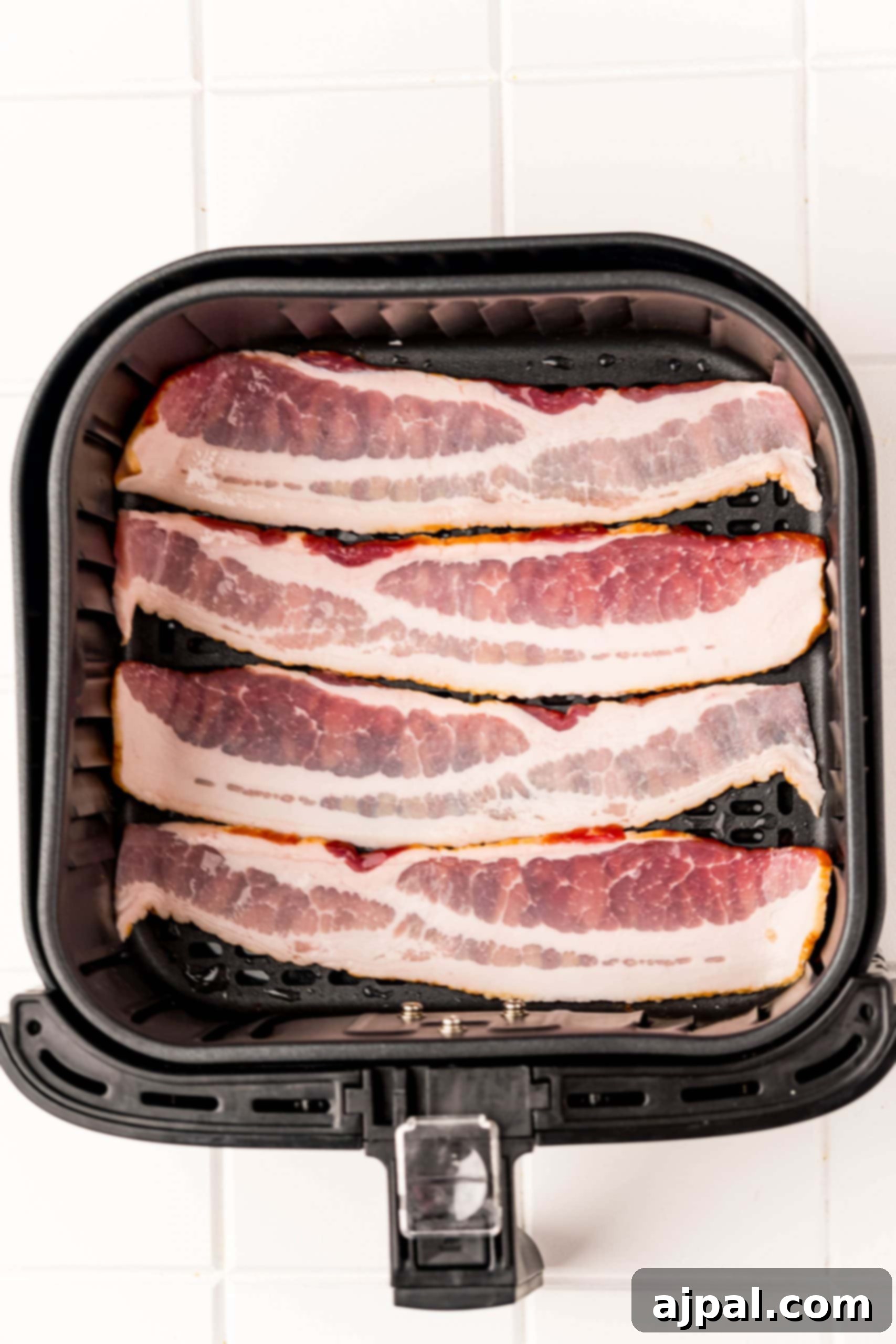 Raw bacon strips arranged neatly in an air fryer basket.