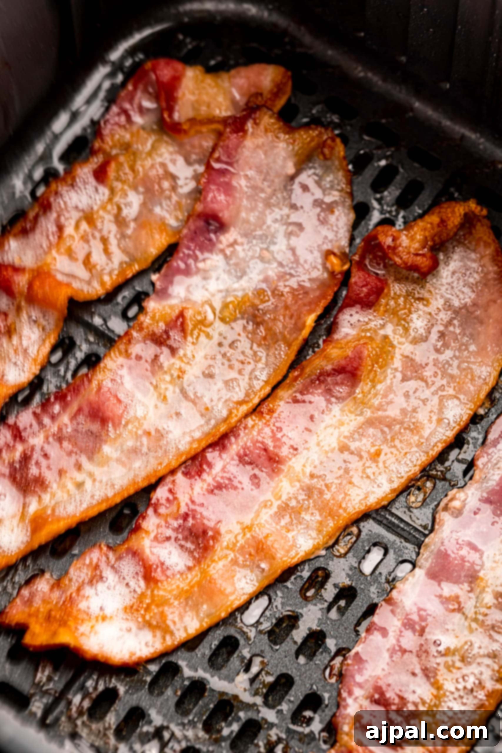 Bacon strips sizzling and cooking inside an air fryer basket.