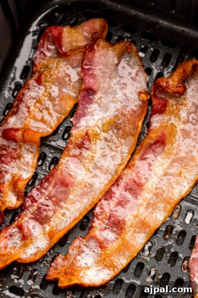 Crispy bacon strips cooking in an air fryer basket, with hints of brown sugar caramelization.