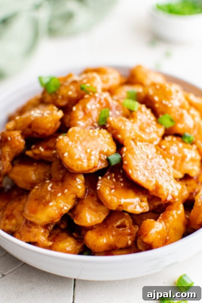 Effortless Sesame Chicken 10 picture of sesame chicken in a bowl over rice, close up, showing the crispy texture and glossy sauce