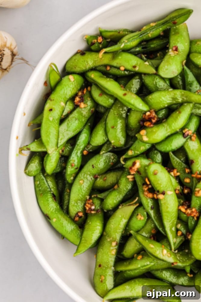 A beautifully arranged bowl of spicy edamame beans, generously seasoned with red pepper flakes and garlic, ready to be enjoyed as a vibrant snack or appetizer.
