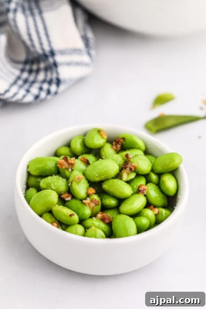 A close-up shot of a white ceramic bowl generously filled with vibrant green edamame beans, lightly seasoned and garnished for serving.