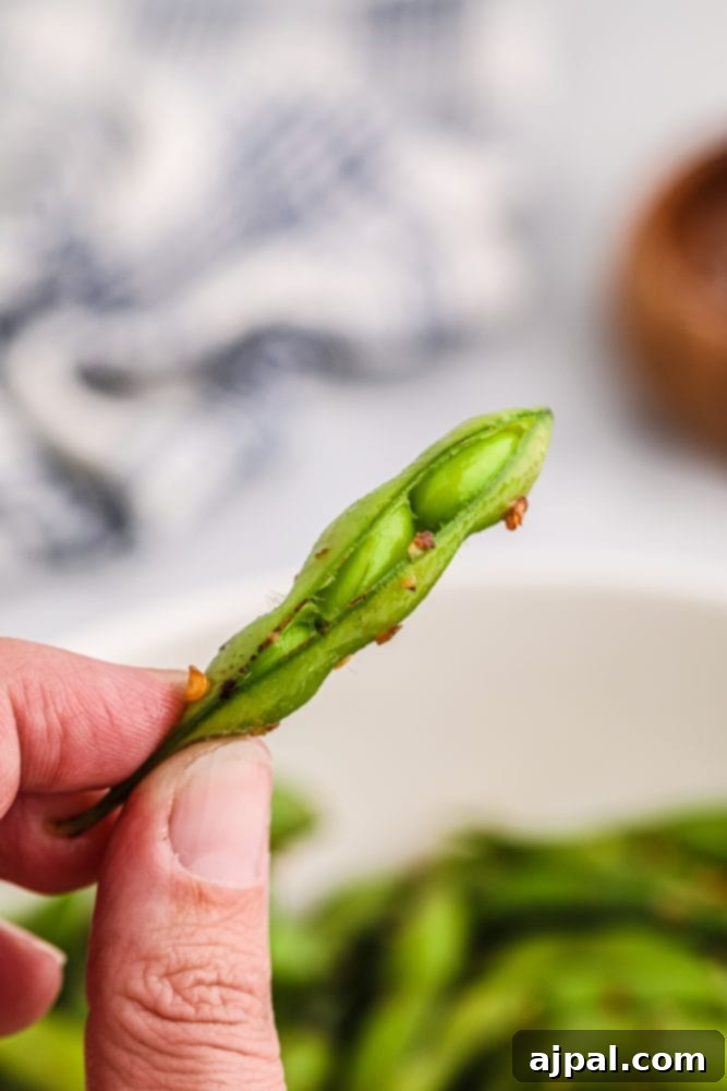 A hand gently holds a spicy edamame bean in its shell, highlighting the vibrant green and seasoning.