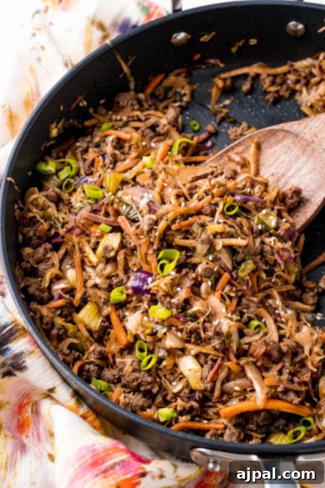 A vibrant keto-friendly egg roll stir-fry simmering in a large skillet, stirred with a wooden spatula, with fresh bok choy visible in the background.