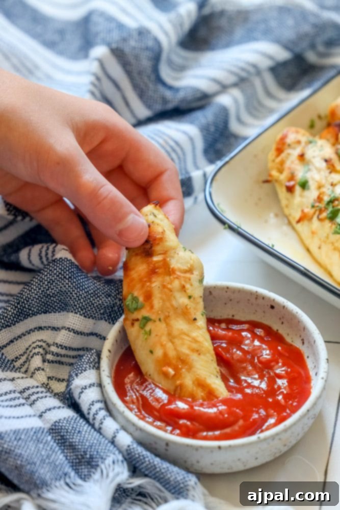 A hand gracefully dipping a savory naked chicken tender into a vibrant bowl of ketchup, showcasing the delicious simplicity of unbreaded air-fried chicken.