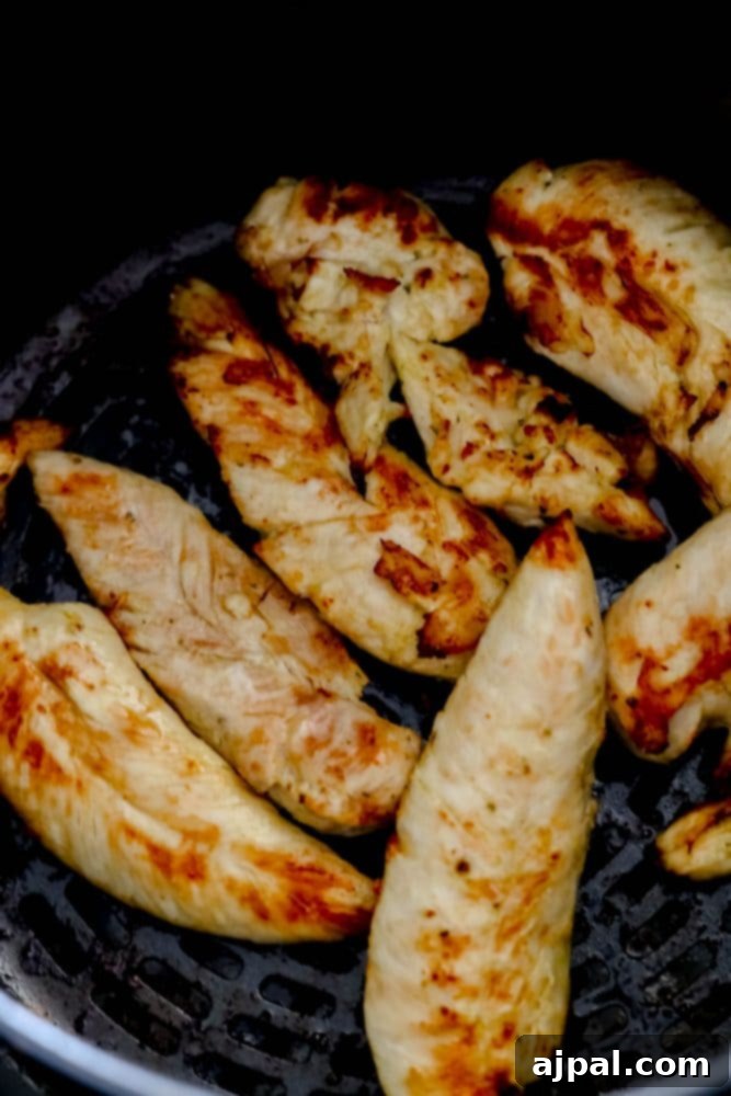 Crispy, golden-brown unbreaded chicken tenders cooking evenly in the basket of an air fryer, highlighting the simplicity of this healthy preparation.