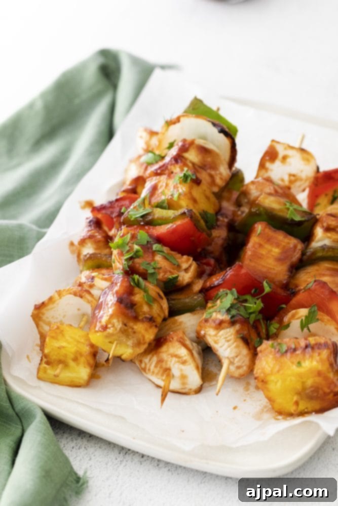Vibrant Hawaiian grilled chicken skewers, featuring golden chicken, bright red and green bell peppers, and sweet pineapple chunks, perfectly arranged on a white plate.