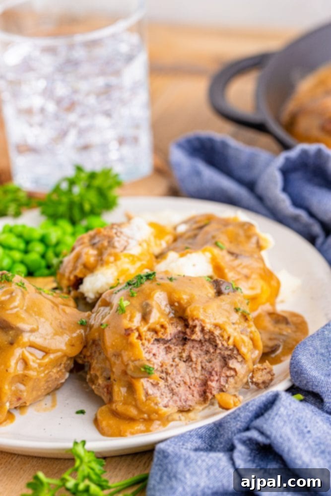 Rich Salisbury Steaks with Velvety Mushroom Gravy 7 A comforting plate featuring Salisbury steak generously coated in mushroom gravy, served with creamy mashed potatoes and vibrant green peas.