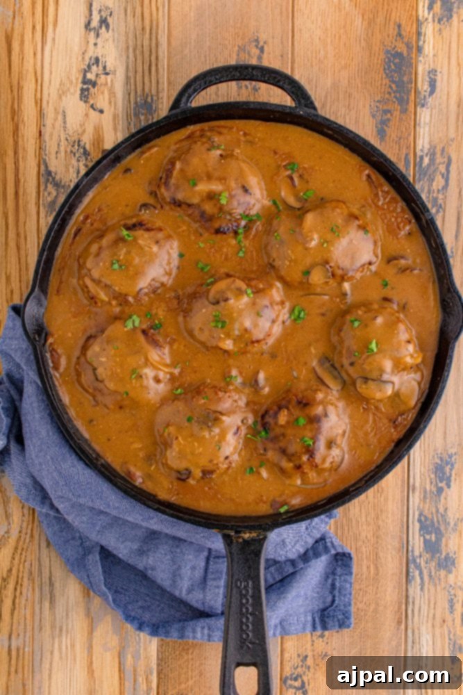Rich Salisbury Steaks with Velvety Mushroom Gravy 4 A bubbling cast iron skillet filled with savory Salisbury steaks submerged in a rich mushroom gravy.