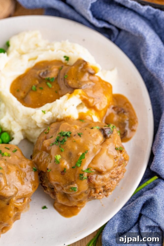 Rich Salisbury Steaks with Velvety Mushroom Gravy 5 A hearty plate of gravy meatloaf, reminiscent of Salisbury steak, served with creamy mashed potatoes and green peas.