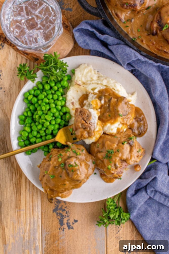 Rich Salisbury Steaks with Velvety Mushroom Gravy 6 A beautifully plated Salisbury steak drenched in brown gravy, accompanied by fluffy mashed potatoes and vibrant green peas.