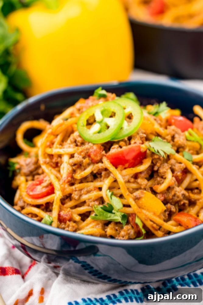 Quick and Delicious Taco Spaghetti 2 A vibrant bowl of cheesy taco spaghetti, topped with ground beef, diced tomatoes, and fresh jalapeños, ready to be enjoyed.