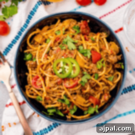 Quick and Delicious Taco Spaghetti 13 A bowl of spicy taco spaghetti, generously topped with ground meat, vibrant sliced jalapeños, cherry tomatoes, and fresh cilantro, presented beautifully on a patterned cloth.