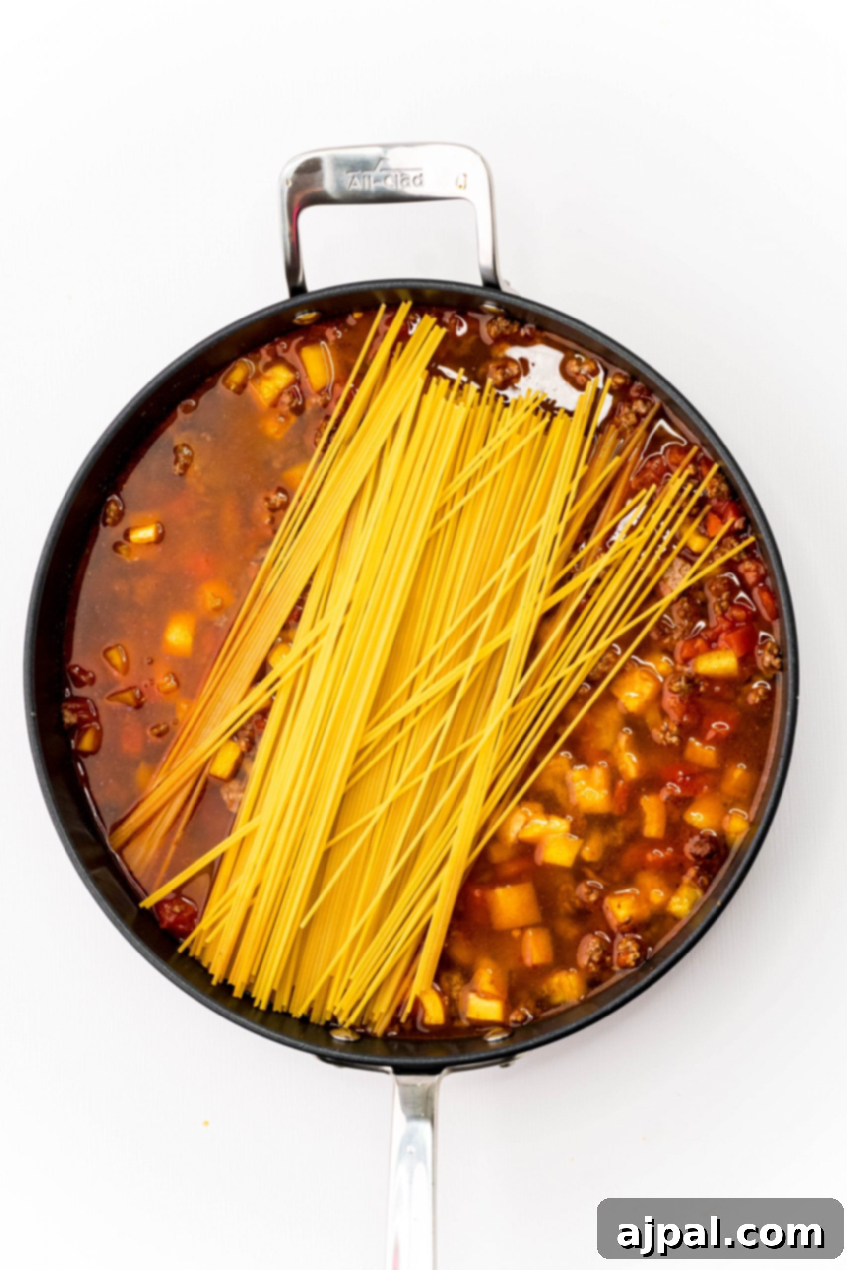 Quick and Delicious Taco Spaghetti 6 A close-up view of cheesy one-pot taco spaghetti cooking in a frying pan, with the melted cheese and seasoned meat prominently featured.