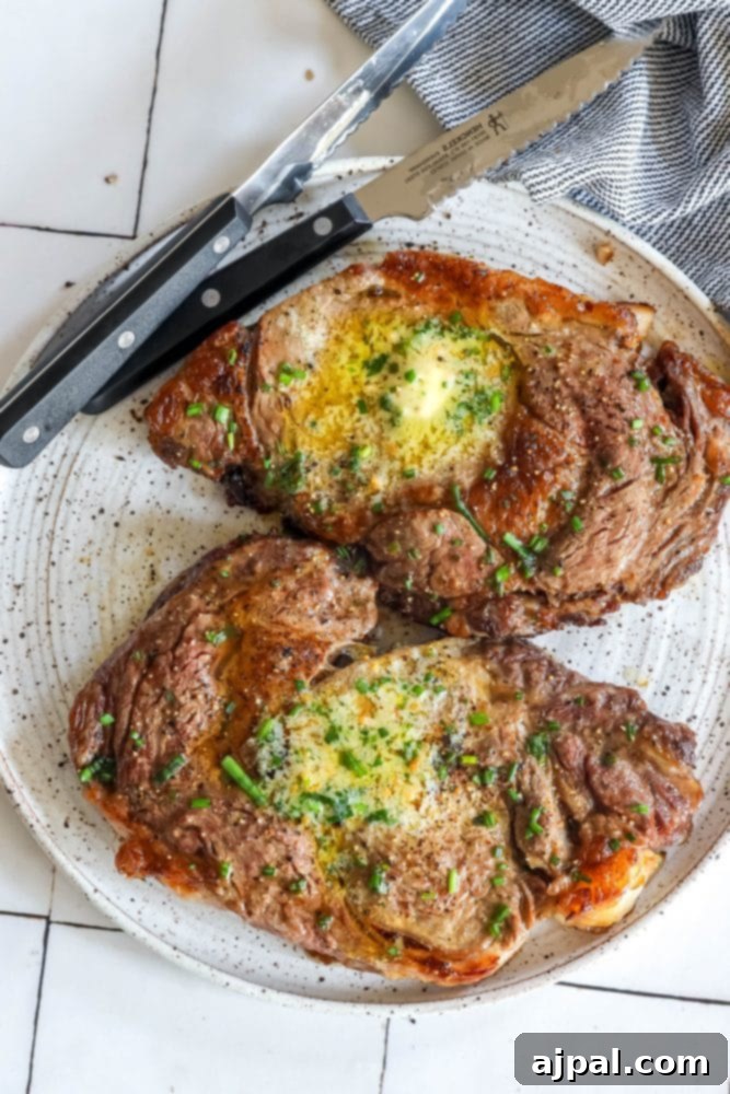 Air Fryer Ribeye Perfection 2 Two perfectly cooked ribeye steaks, garnished with fresh herbs, resting on a serving plate with a steak knife.