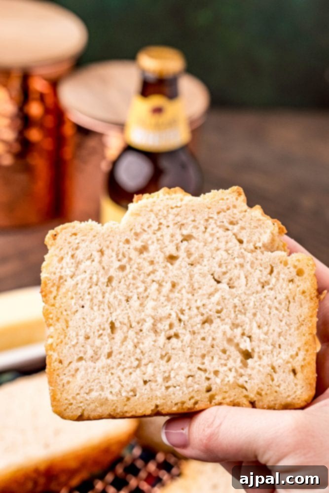 A hand holding a slice of golden-brown beer bread, showcasing its inviting texture and warmth.