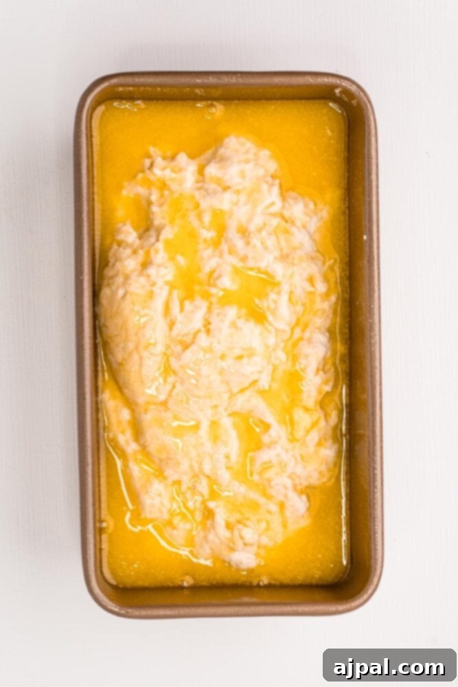 Melted butter generously poured over the beer bread dough in the loaf pan, promising a golden crust.