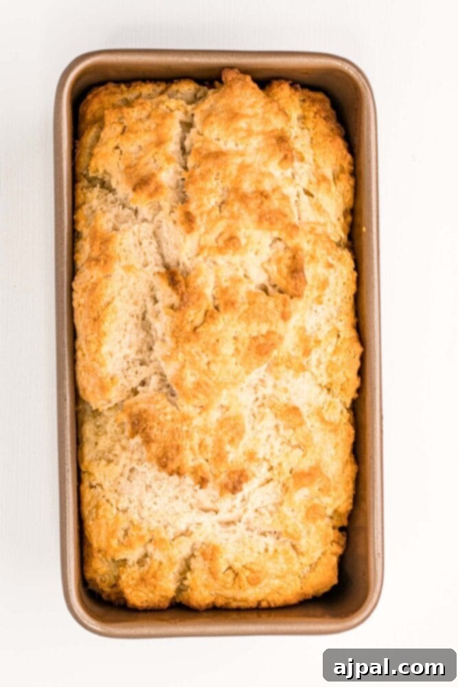 Freshly baked beer bread cooling in its loaf pan, showing off its perfectly golden-brown crust.