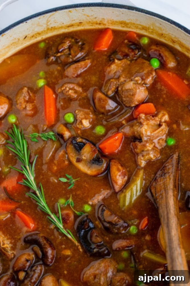 A steaming bowl of rich venison stew in a rustic Dutch oven, showcasing tender meat and colorful vegetables.