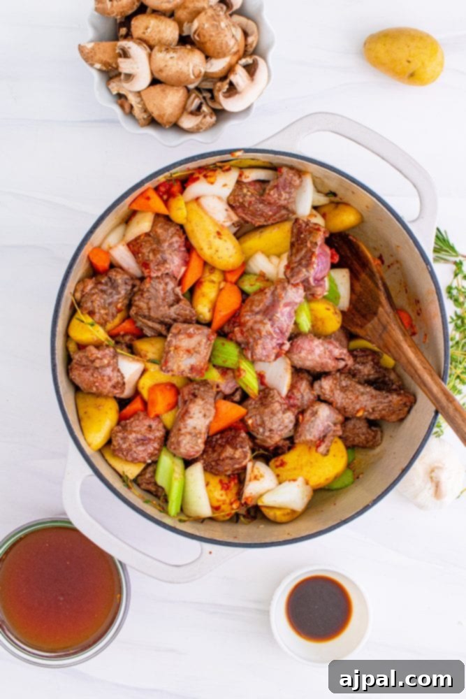 Cooked venison meat and browned vegetables combined in a large pan, ready for simmering.